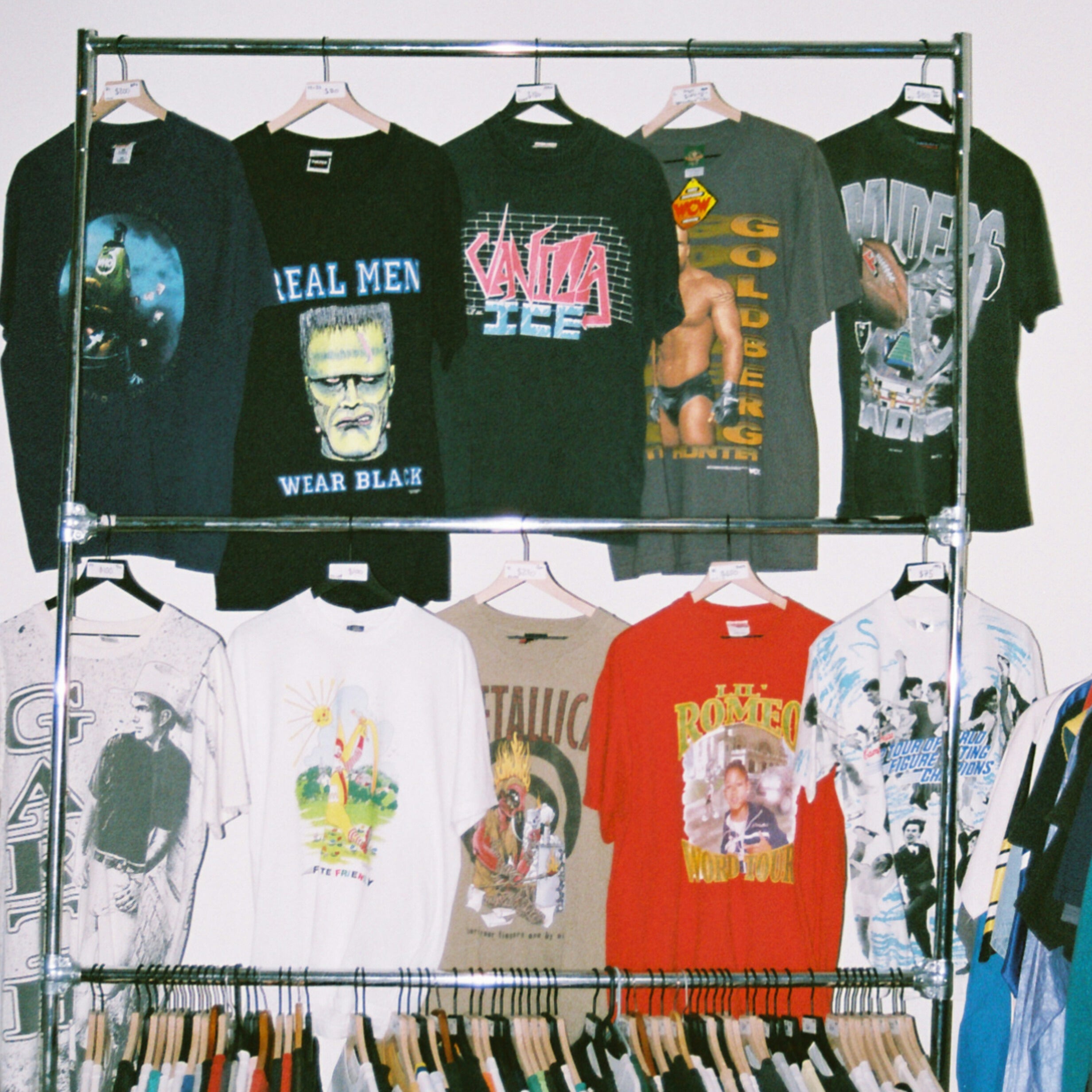 a collection of vintage t-shirts hung up on a metal rail featuring some classic bands, artists and famous sportsmen